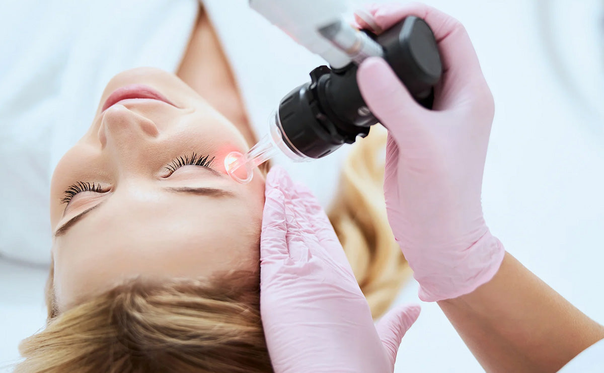 woman lying on a treatment bed with a person wearing gloves applying a laser-like tool to her face