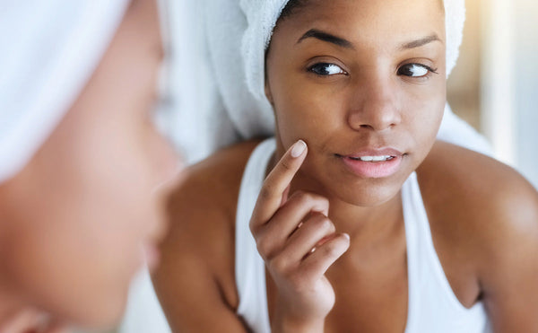 a woman with a towel on her head looking at herself in the mirror, pointing to her cheek with her finger