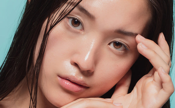a woman facing the camera with clear, wet skin, as if she has applied some skincare product, indicating a fresh and glowing complexion