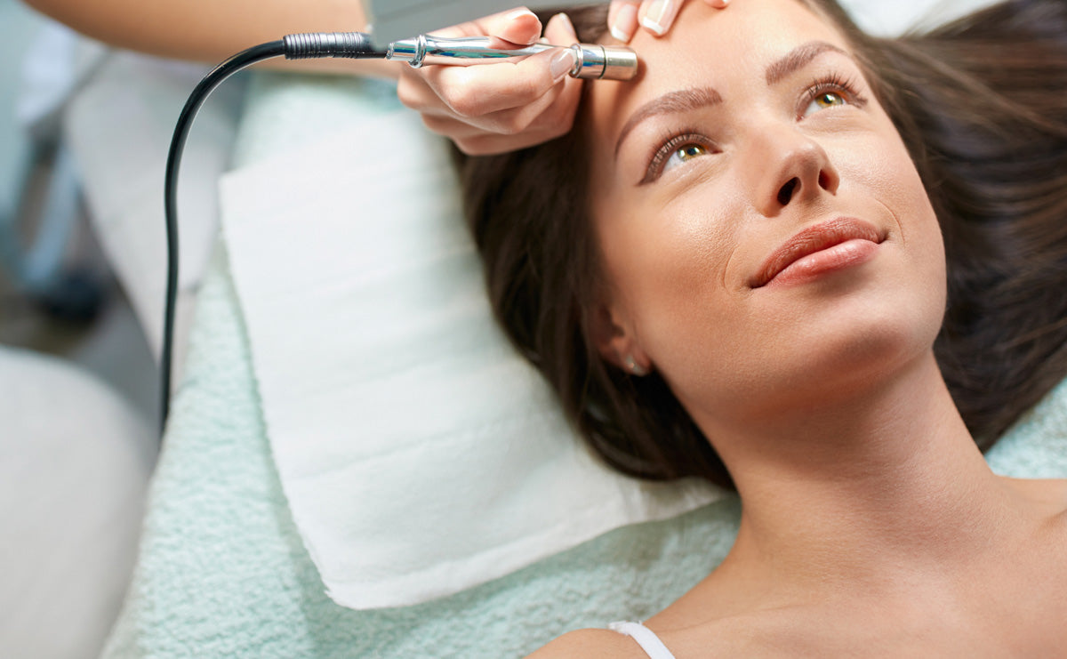 a woman lying on a treatment bed receiving a microdermabrasion treatment from an aesthetic provider