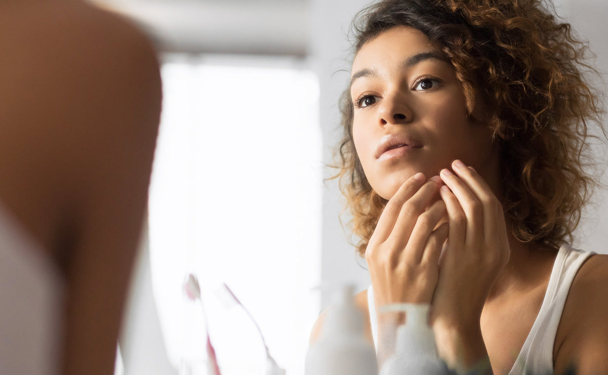 a woman looking thoughtfully into a mirror, preparing to apply RescueMD serum on her face