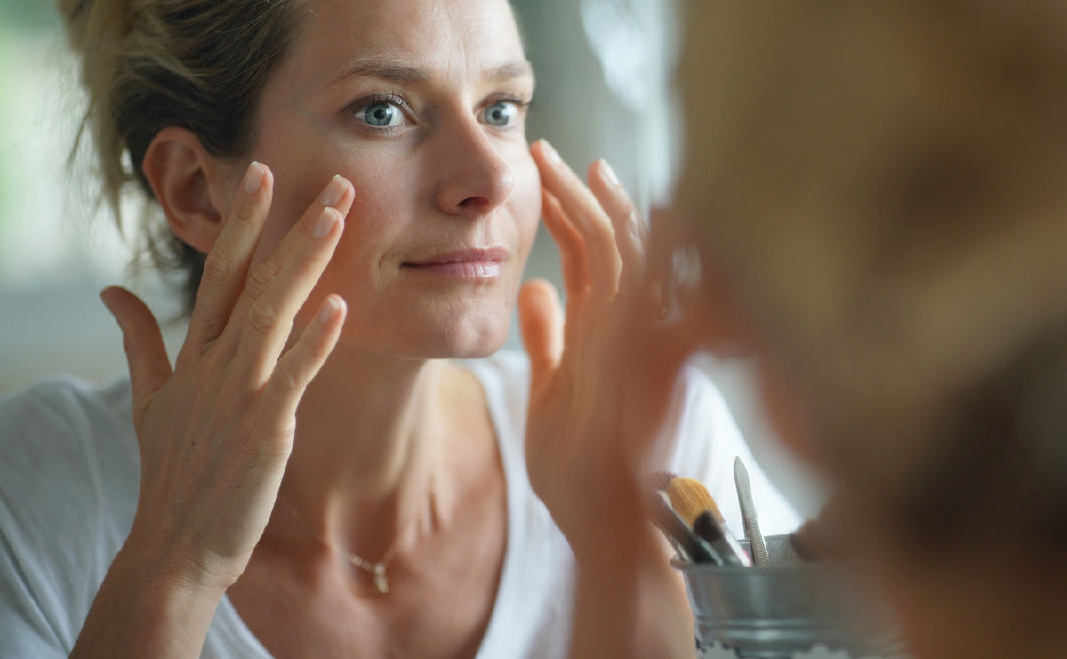 a woman with gray eyes looking into the mirror and applying RescueMD serum on her face
