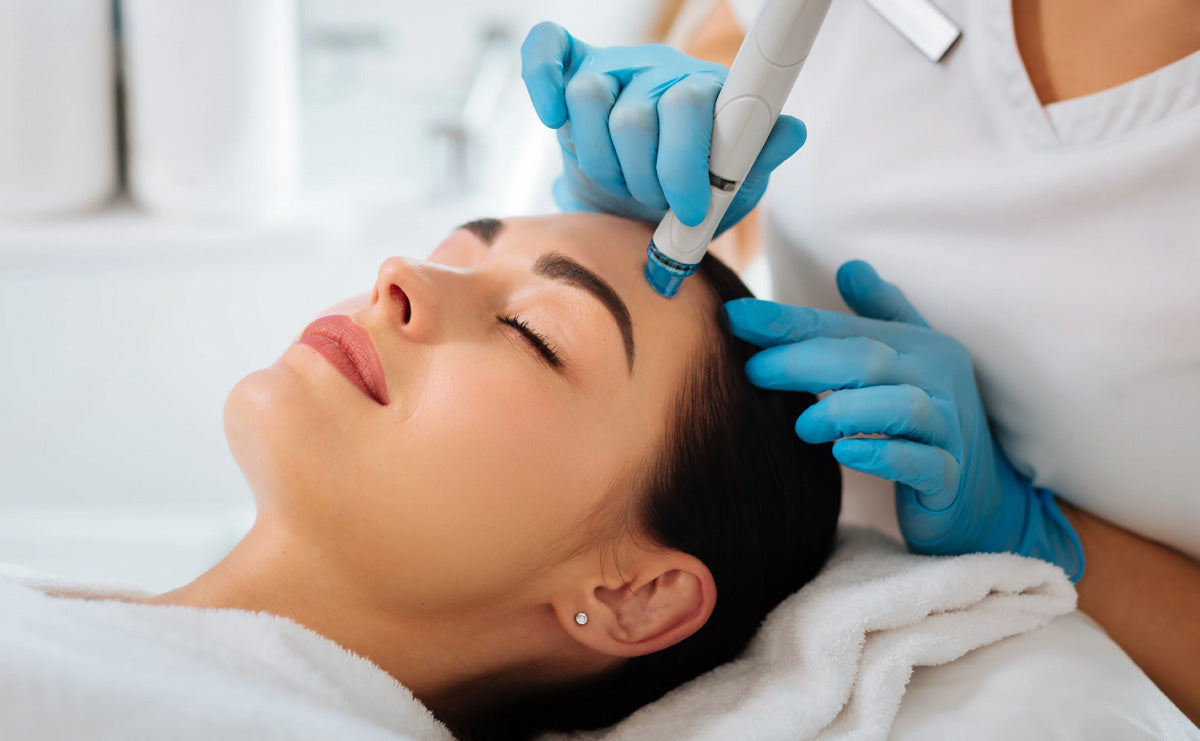 a woman lying on a treatment bed receiving skin therapy on her skin near her forehead