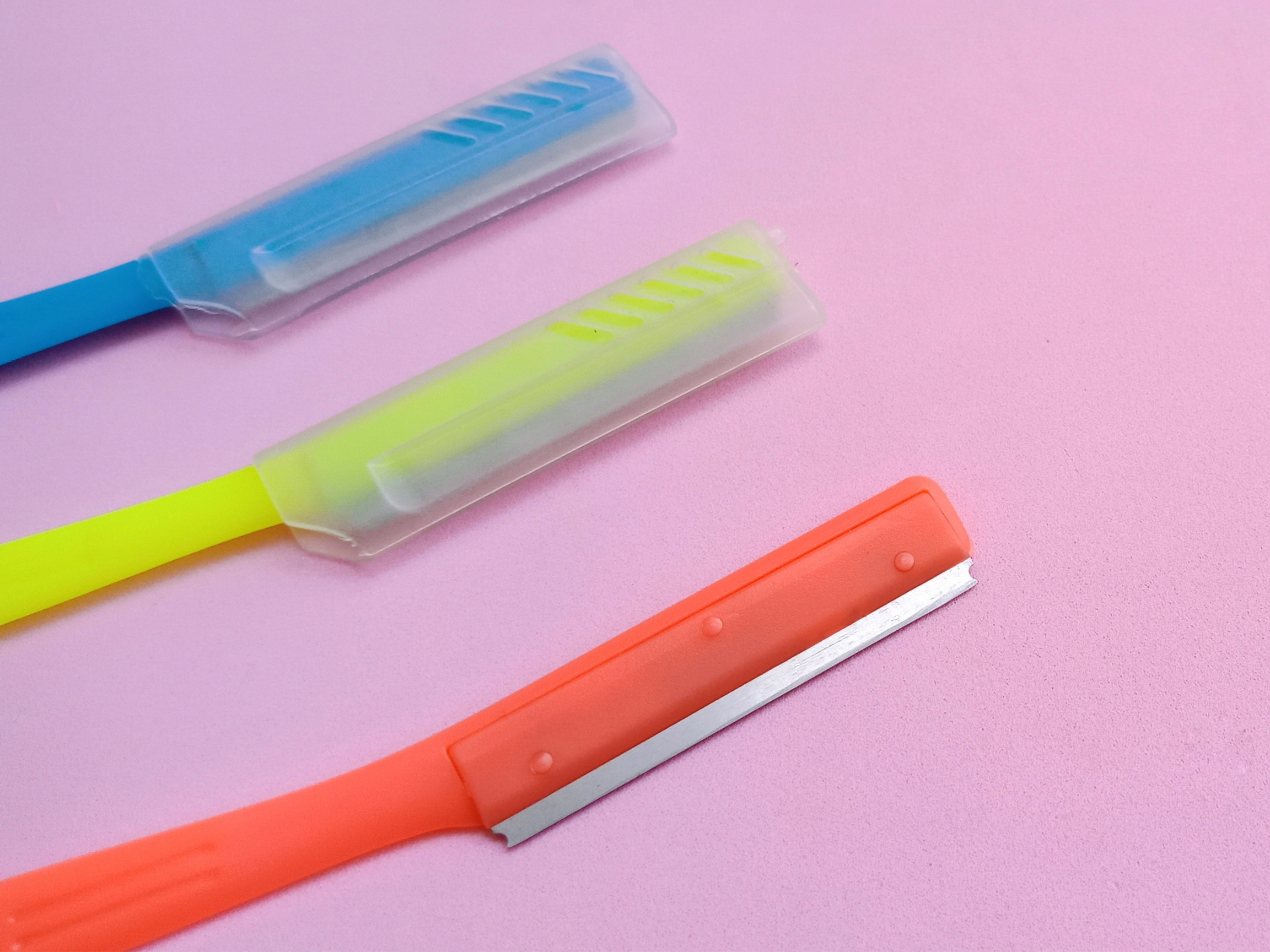 close-up of three facial razors on pink surface