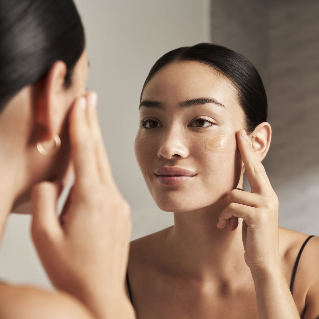 a woman looking in the mirror while applying RescueMD serum on her face